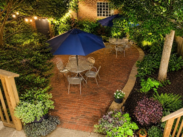 A patio with a brick floor, metal chairs, a round table, and a blue umbrella.