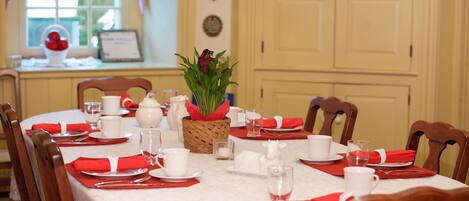 Una mesa de comedor lista para una comida, con servilletas rojas, platos blancos y vasos transparentes.