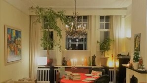 Uma sala de estar acolhedora com área de jantar, apresentando um candelabro, lareira e uma grande janela com cortinas.