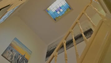 Una escalera con barandilla de madera que lleva a una habitación con un cuadro de la ciudad y un vitral.