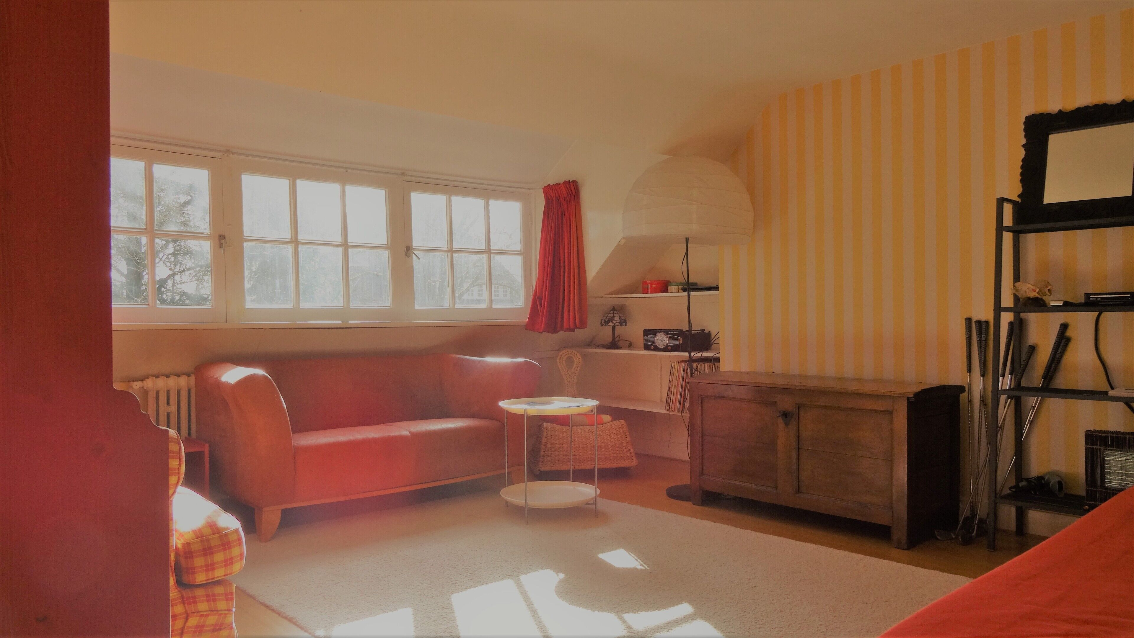 Una sala de estar con un sofá rojo, una mesa redonda pequeña, un mueble aparador y una estantería.