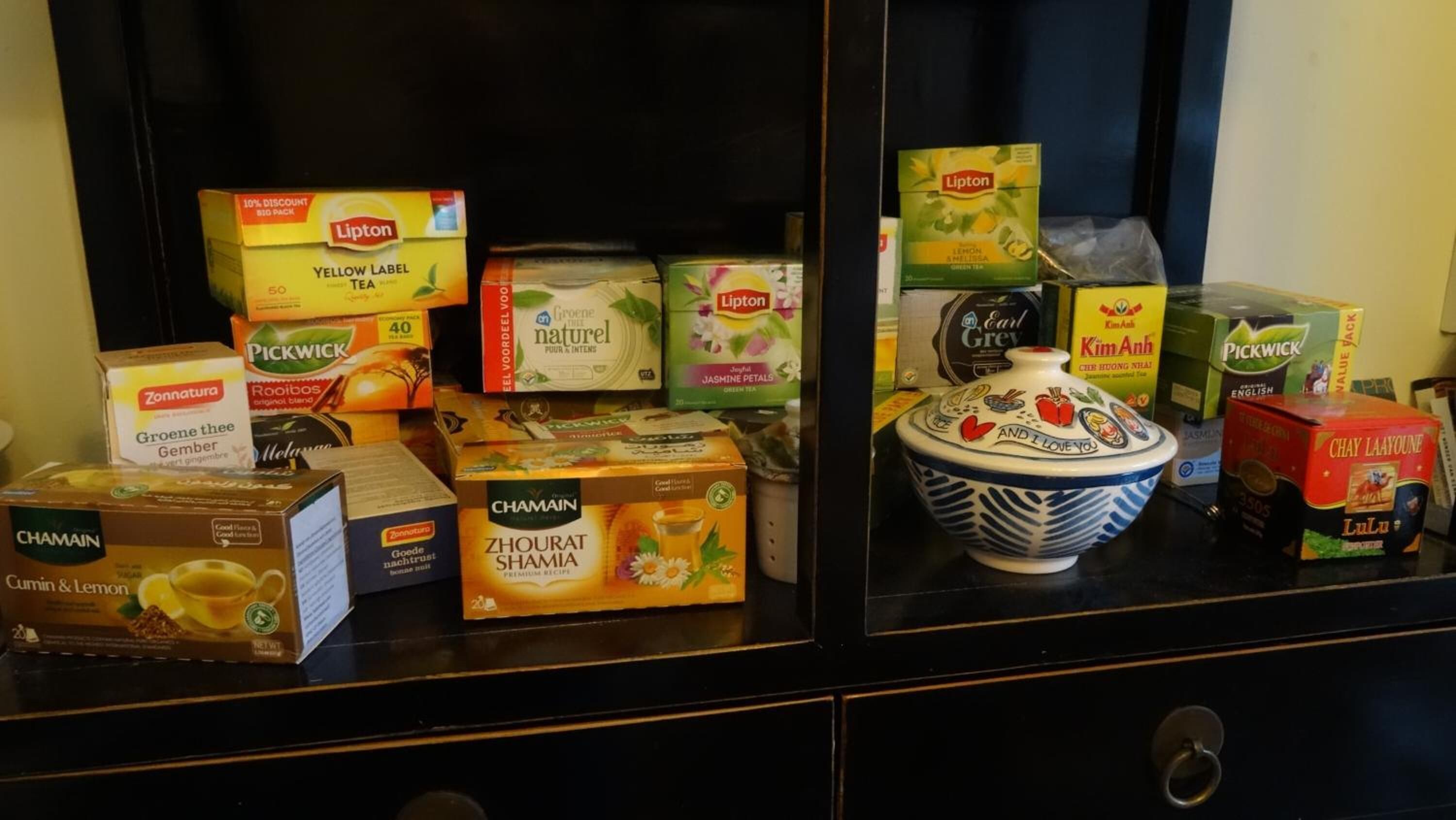 A variety of tea boxes and a decorative bowl on a shelf.