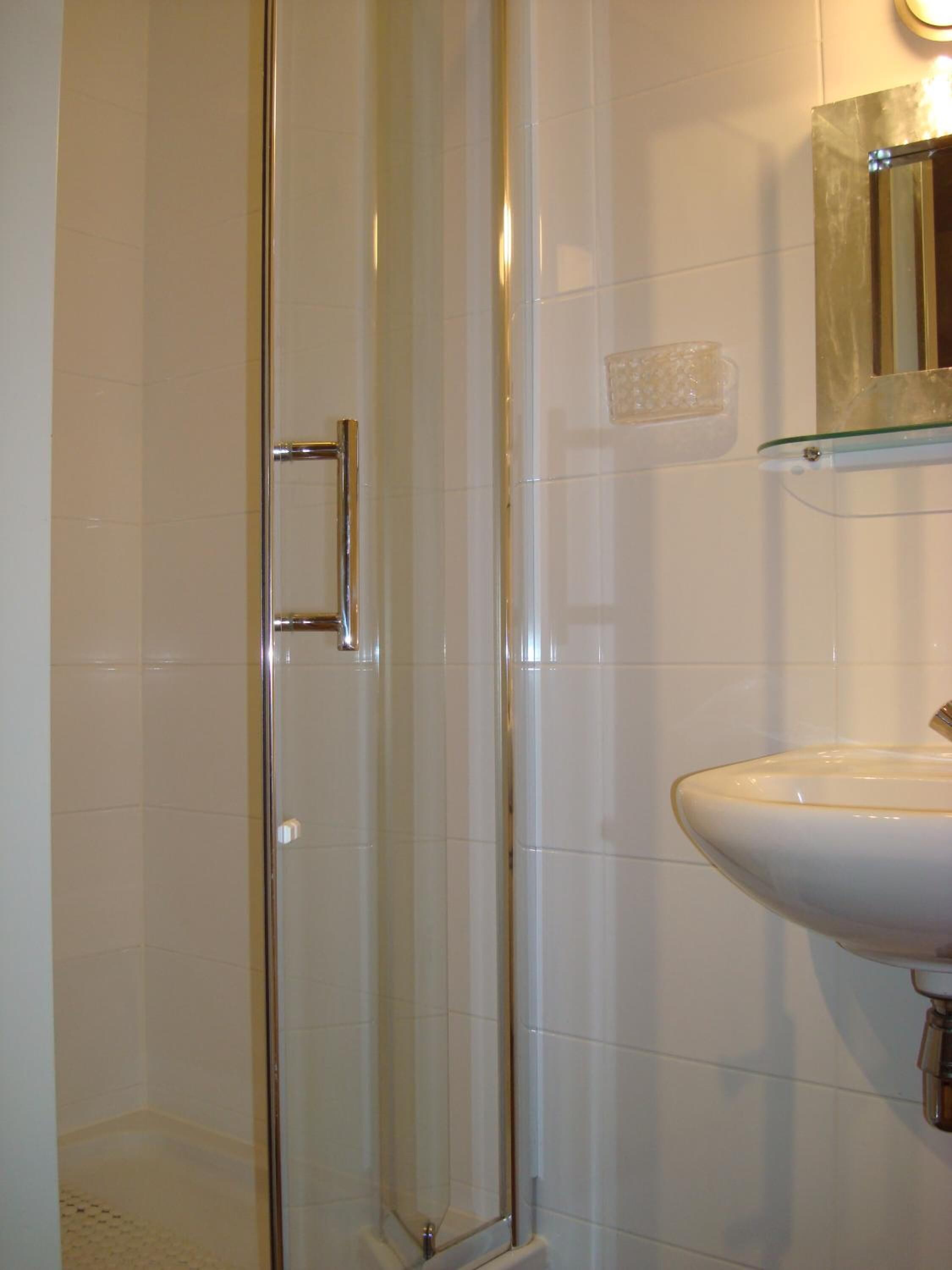Un baño con cabina de ducha de vidrio, un lavabo blanco y un espejo sobre él.