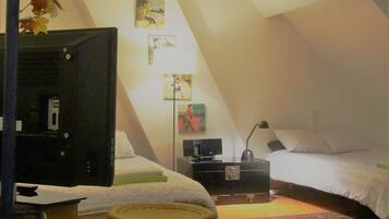 Un dormitorio acogedor en el ático con una cama, un televisor, una mesita pequeña y una planta decorativa.