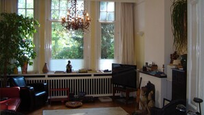 Ein Wohnzimmer mit großem Fenster, einer Kandelaberleuchte, einem Fernseher und verschiedenen Dekorationsgegenständen.