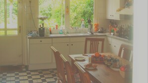 Uma cozinha com piso xadrez, cadeiras de madeira, mesa de jantar e janela com vista para o verde.