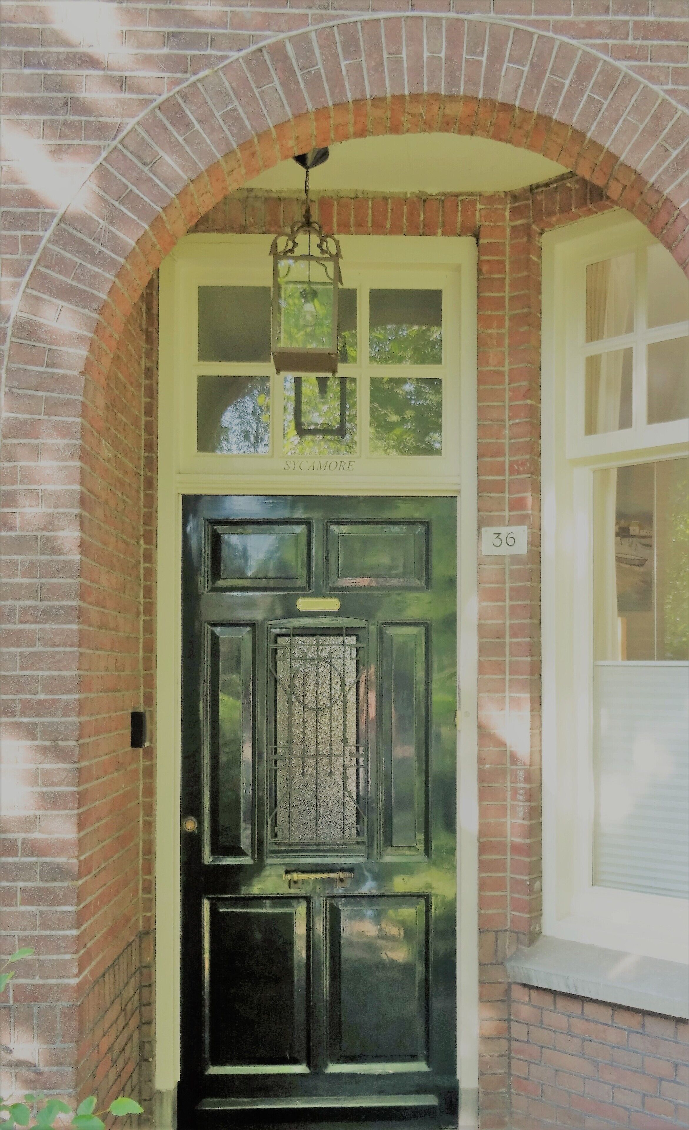Una puerta negra con un panel de vidrio decorativo, un farol colgante y un arco de ladrillo.