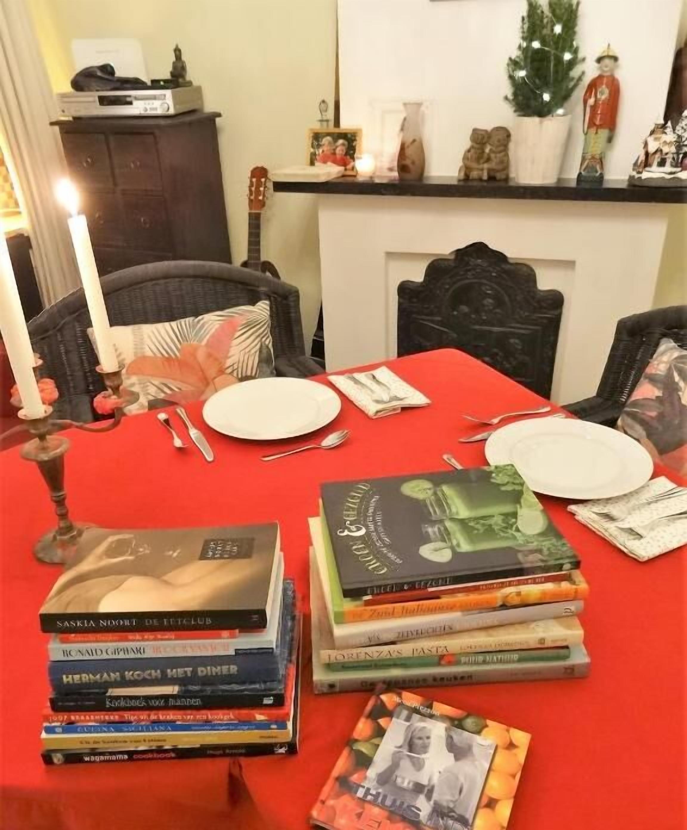 A dining table set with plates, cutlery, and a stack of books.