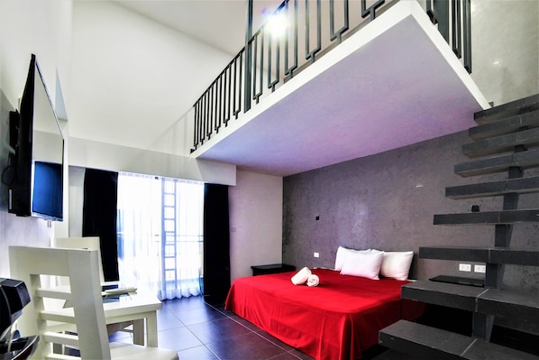 A modern hotel room with a bed, a desk, a chair, and a staircase.