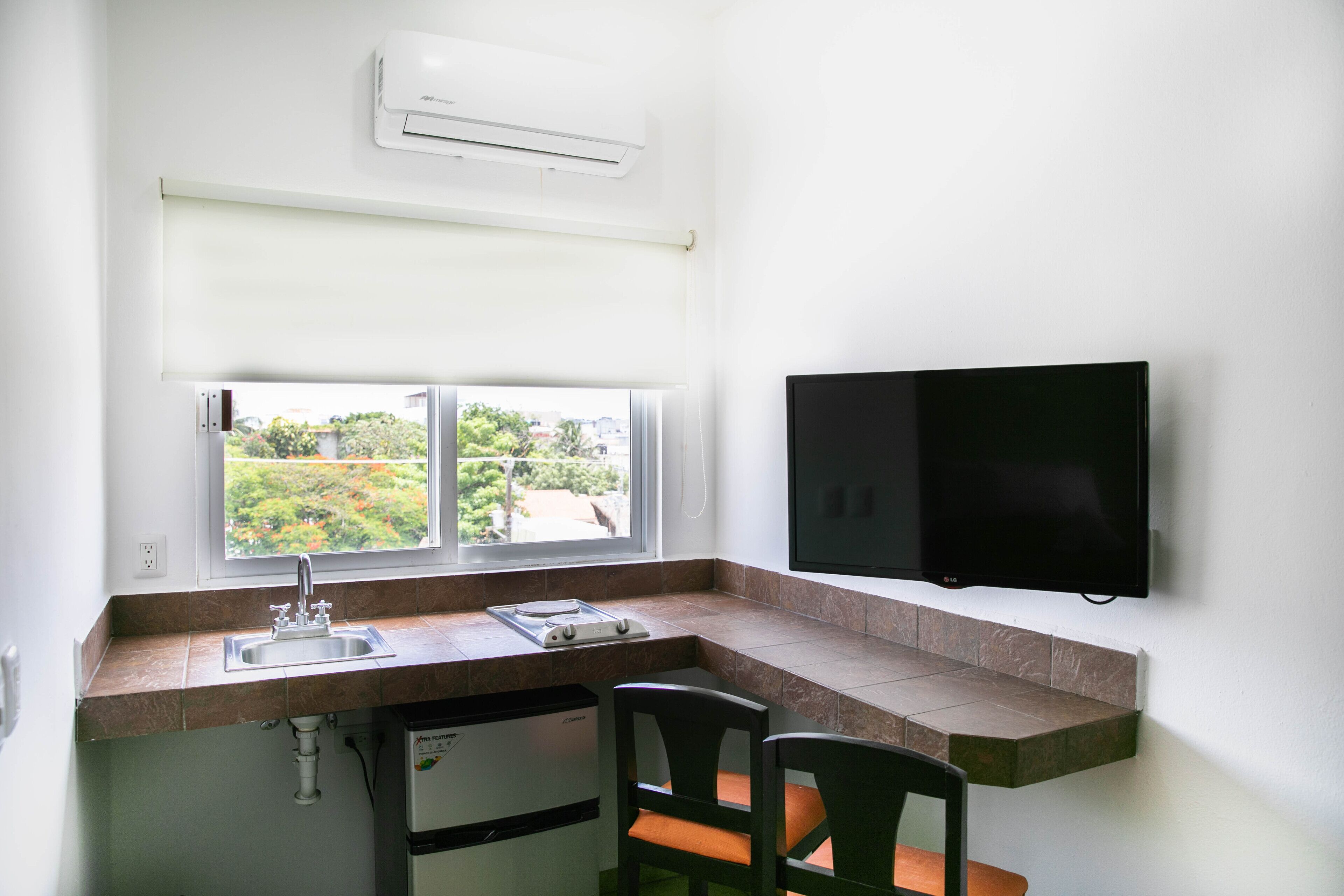 A compact kitchen with a window, sink, and a flat-screen TV.