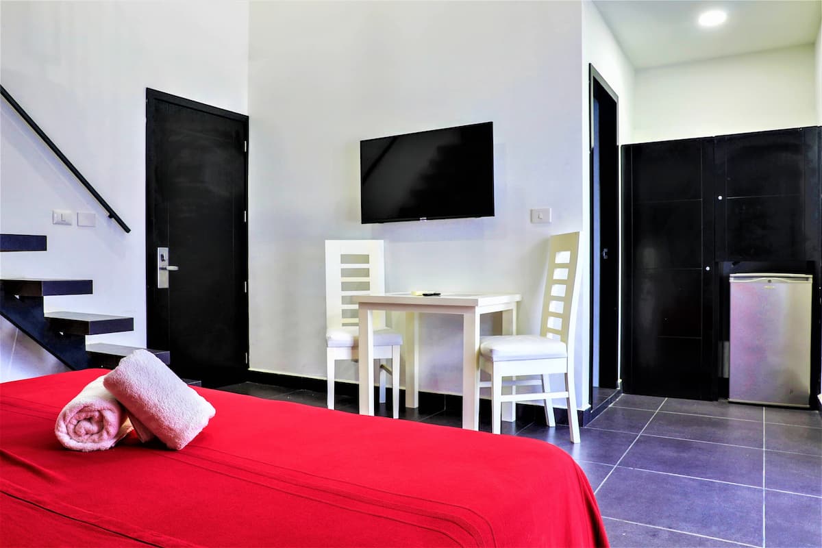 Habitación de hotel con cama, escritorio, dos sillas, televisor y refrigerador.