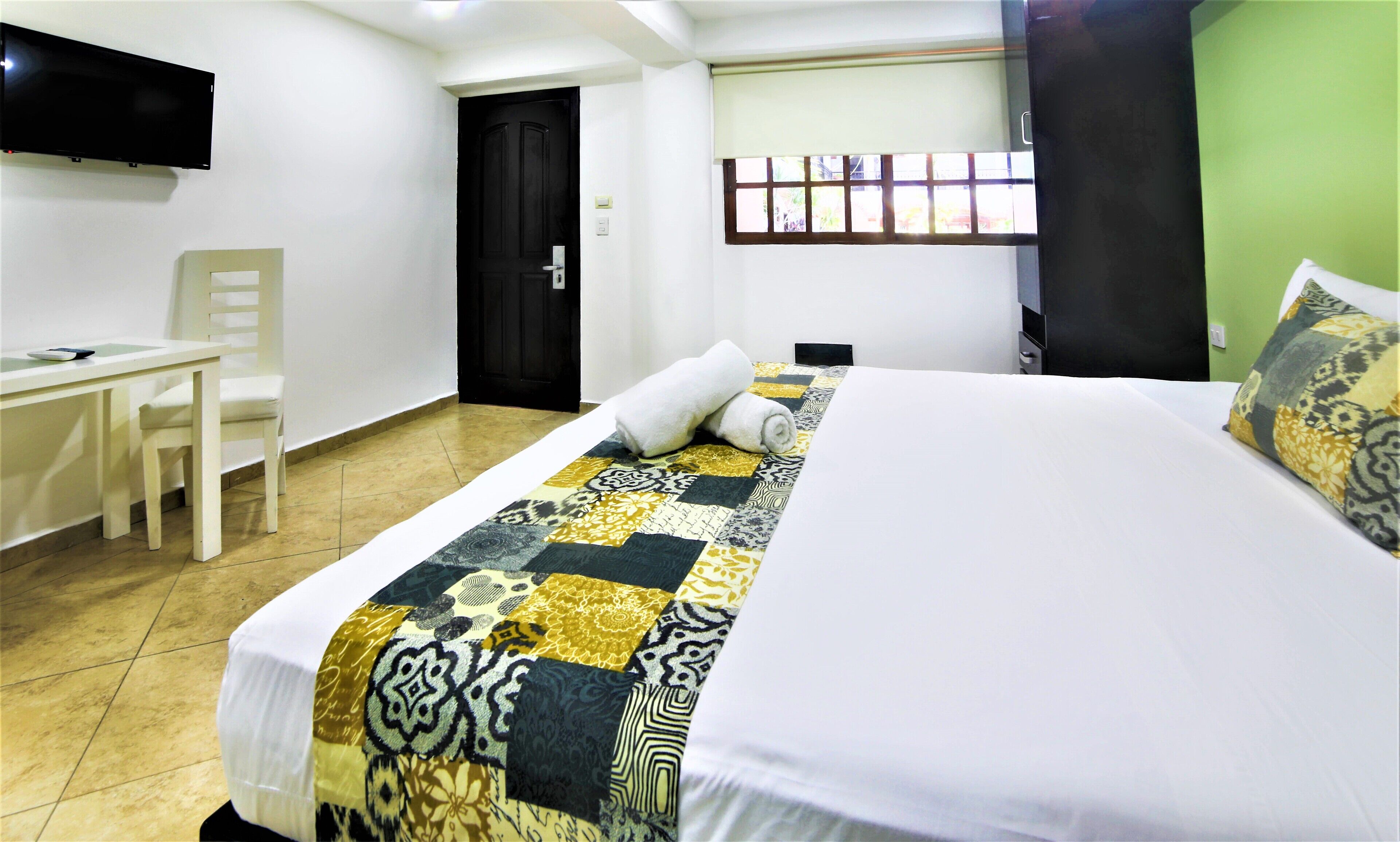 A hotel room with a bed, a desk, a chair, a television, and a window.