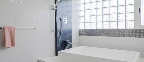 A modern bathroom with a white bathtub, a shower area, and a window with a grid pattern.