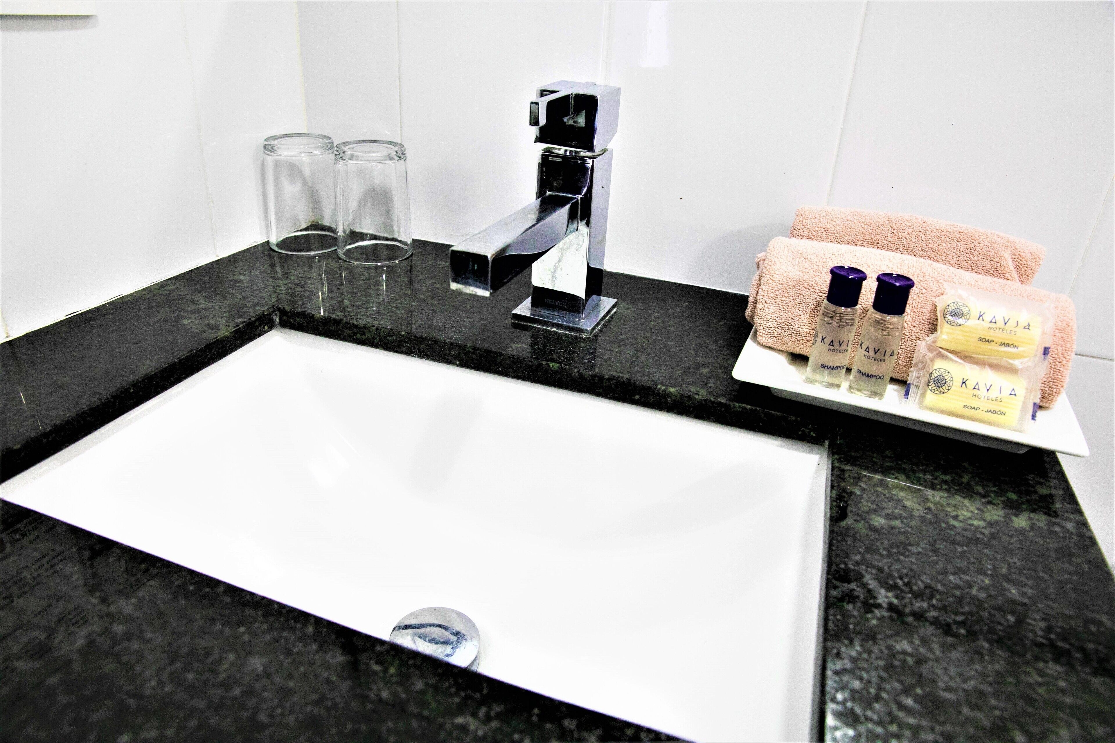 Un lavabo de salle de bain avec un robinet chromé, deux verres transparents et un porte-serviettes avec des serviettes et des articles de toilette.