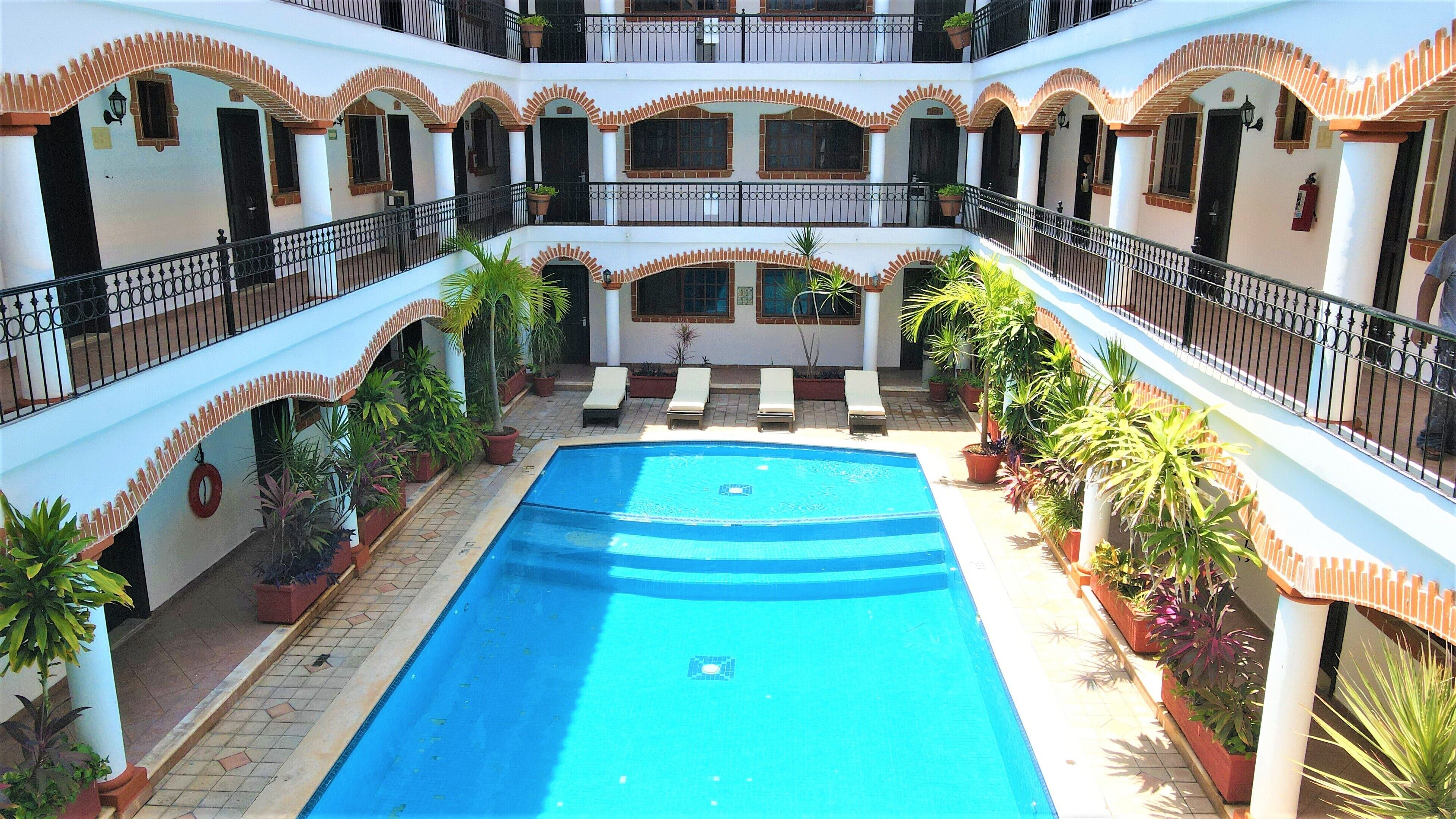A multi-level building with a central swimming pool surrounded by potted plants and lounge chairs.