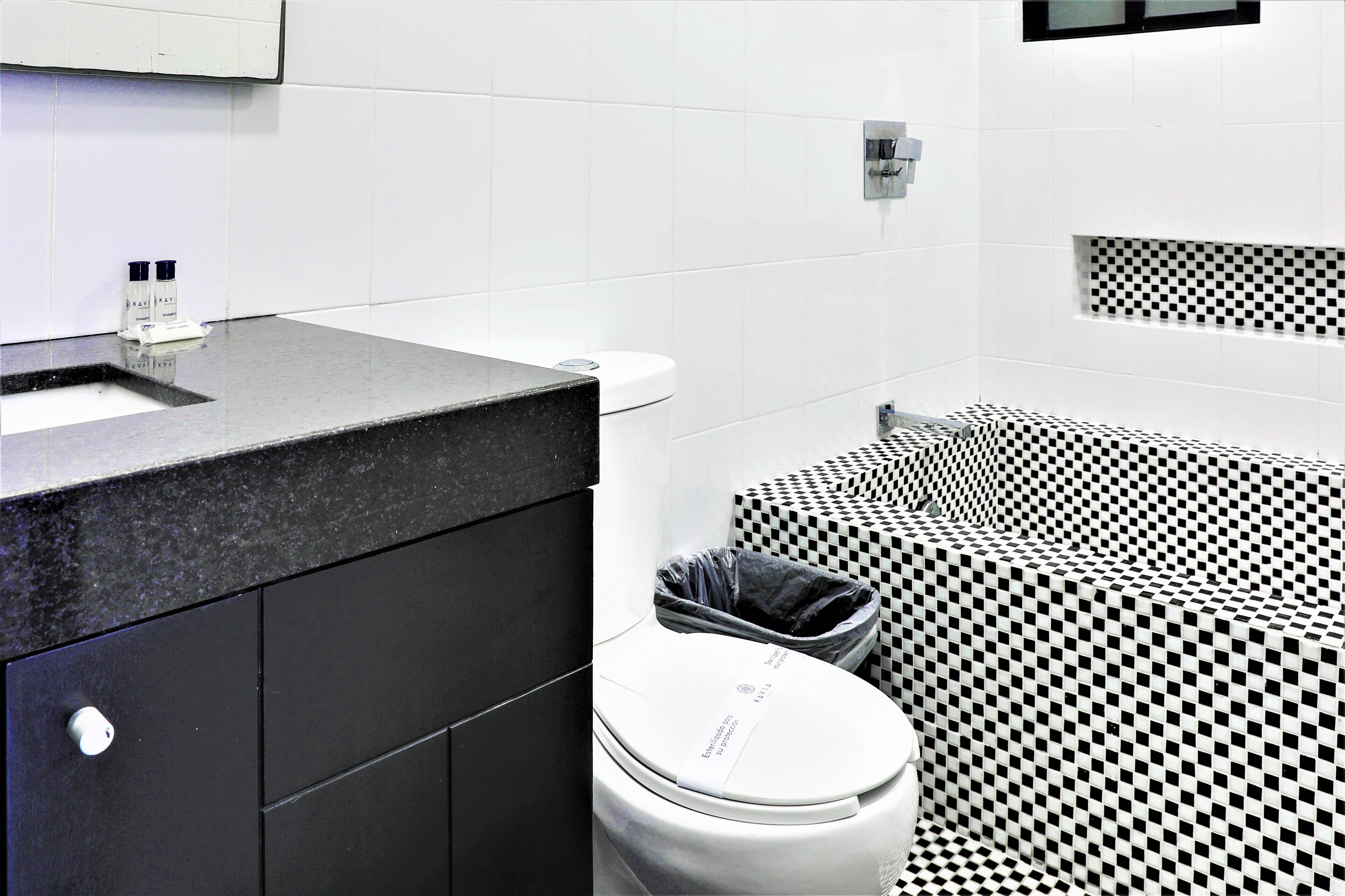 Un baño moderno con piso a cuadros blanco y negro, un inodoro blanco y un mostrador negro con un lavabo.