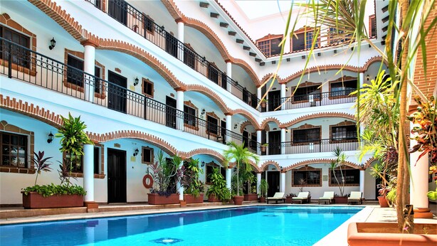 A multi-level hotel with a central swimming pool, balconies, and potted plants.