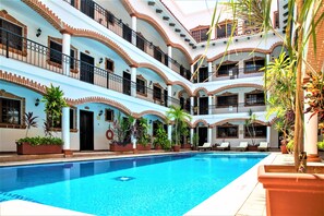 A multi-level hotel with a central swimming pool, balconies, and potted plants.