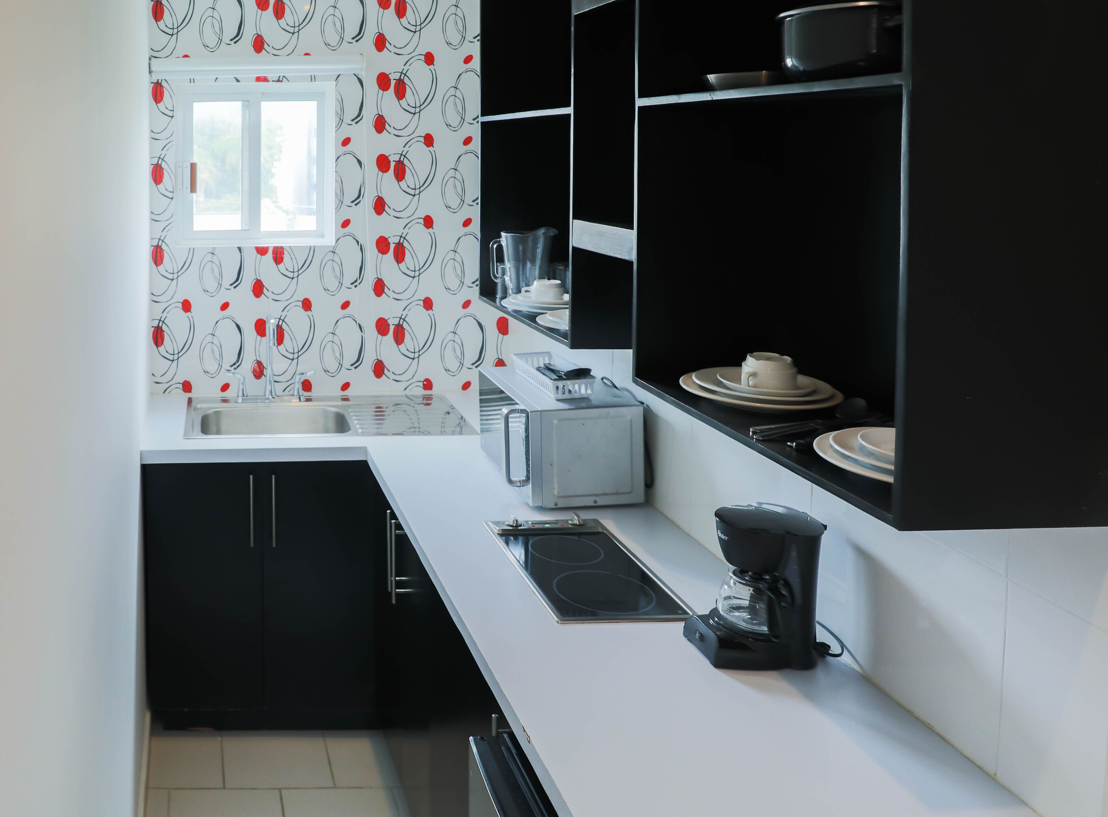 Une cuisine moderne avec des meubles noirs, un plan de travail blanc, un four encastré, une machine à café et une fenêtre donnant sur l’extérieur.