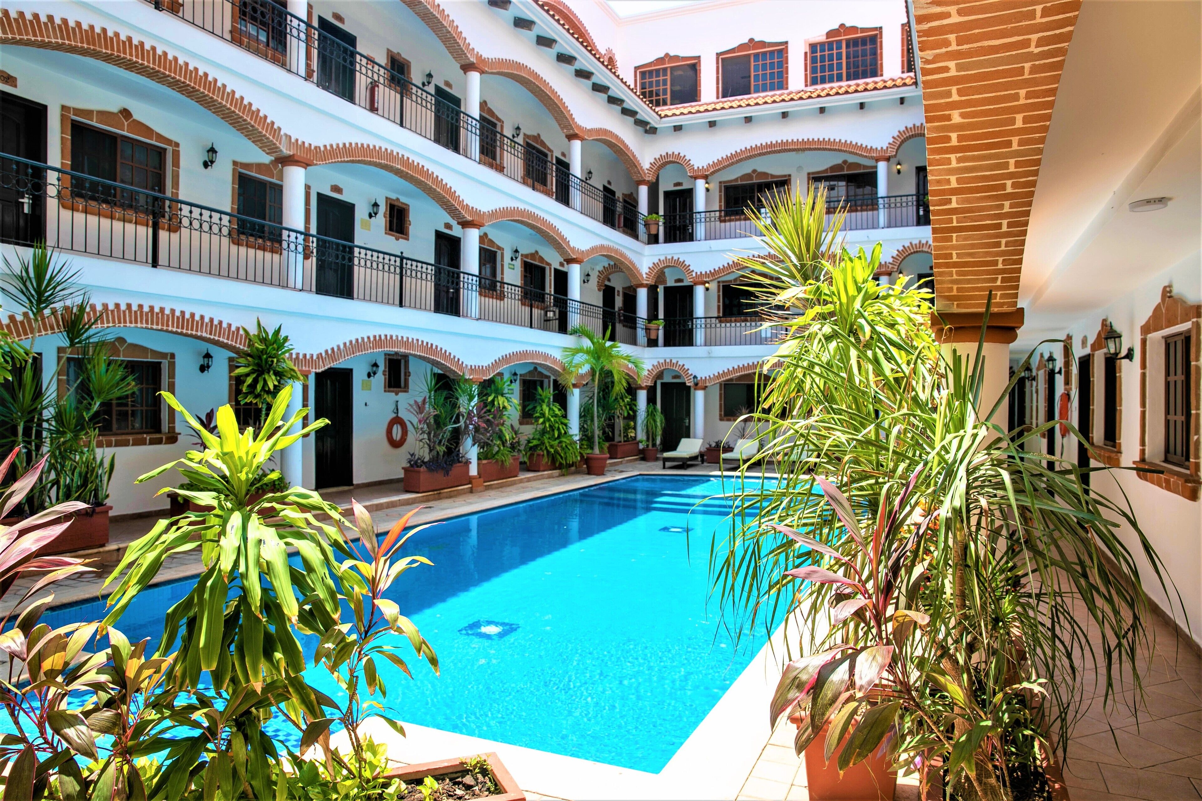 A multi-story hotel with a central swimming pool surrounded by potted plants.