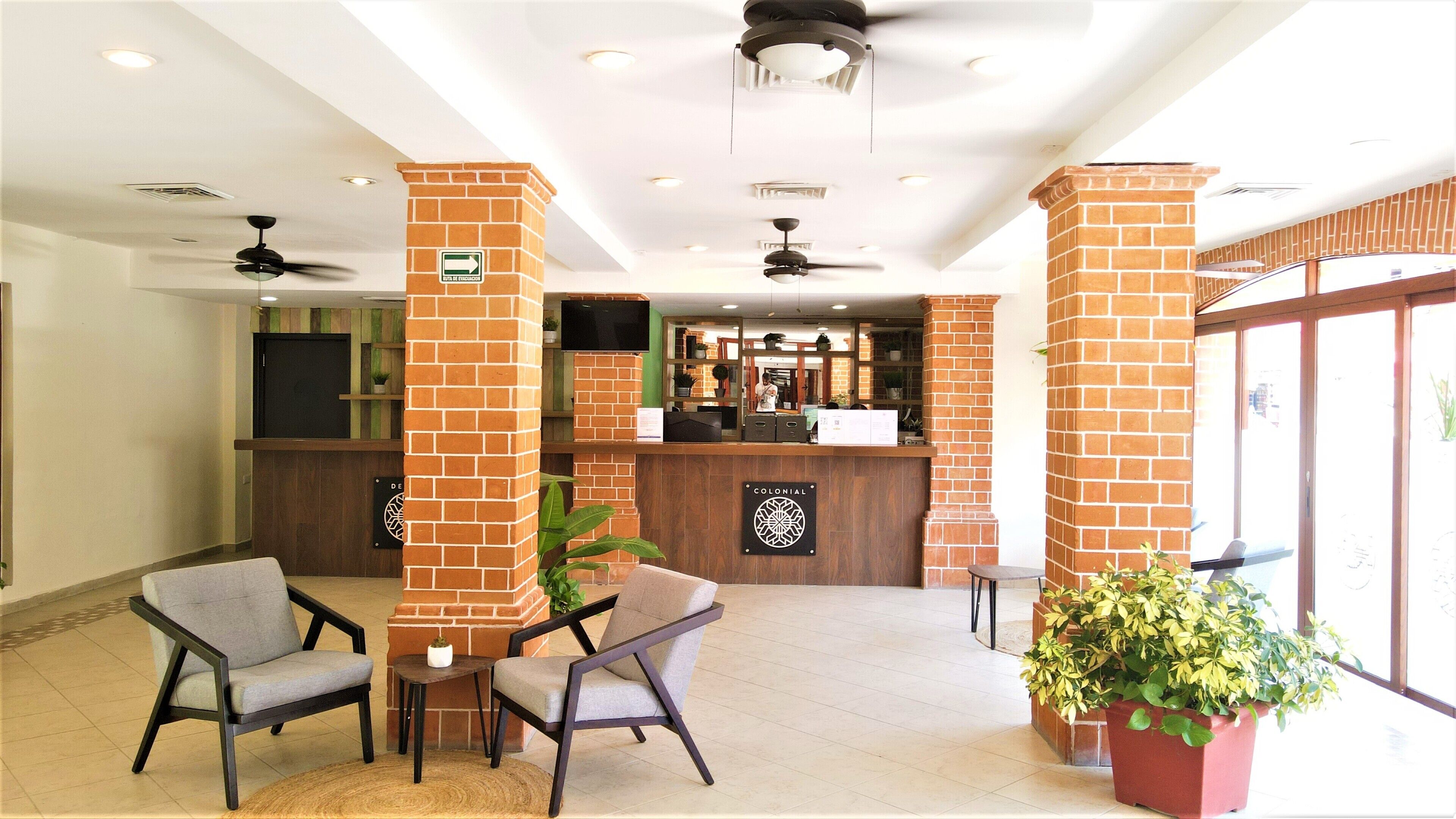 A lobby with brick pillars, a reception desk, and seating area with chairs and a table.