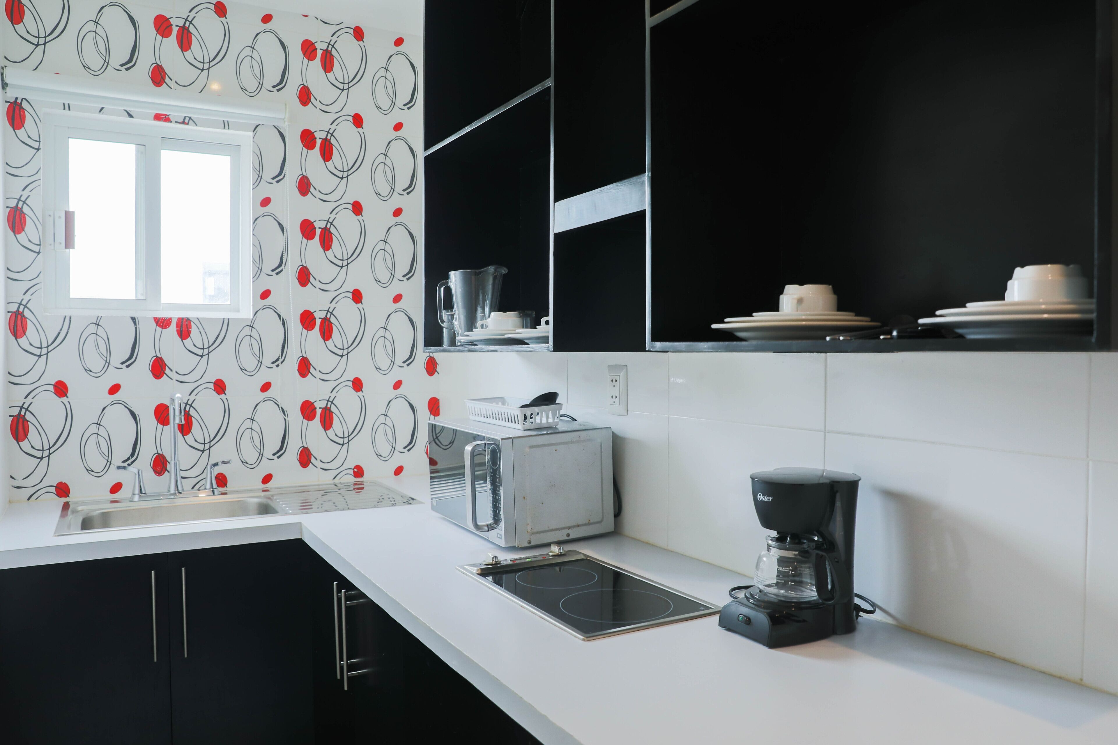 A modern kitchen with a black and white color scheme, a built-in oven, a coffee maker, and a window above the sink.