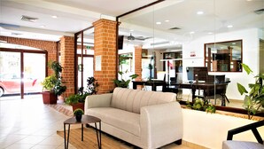 A lobby with a sofa, a small table, and a chair. There are potted plants and a brick pillar.