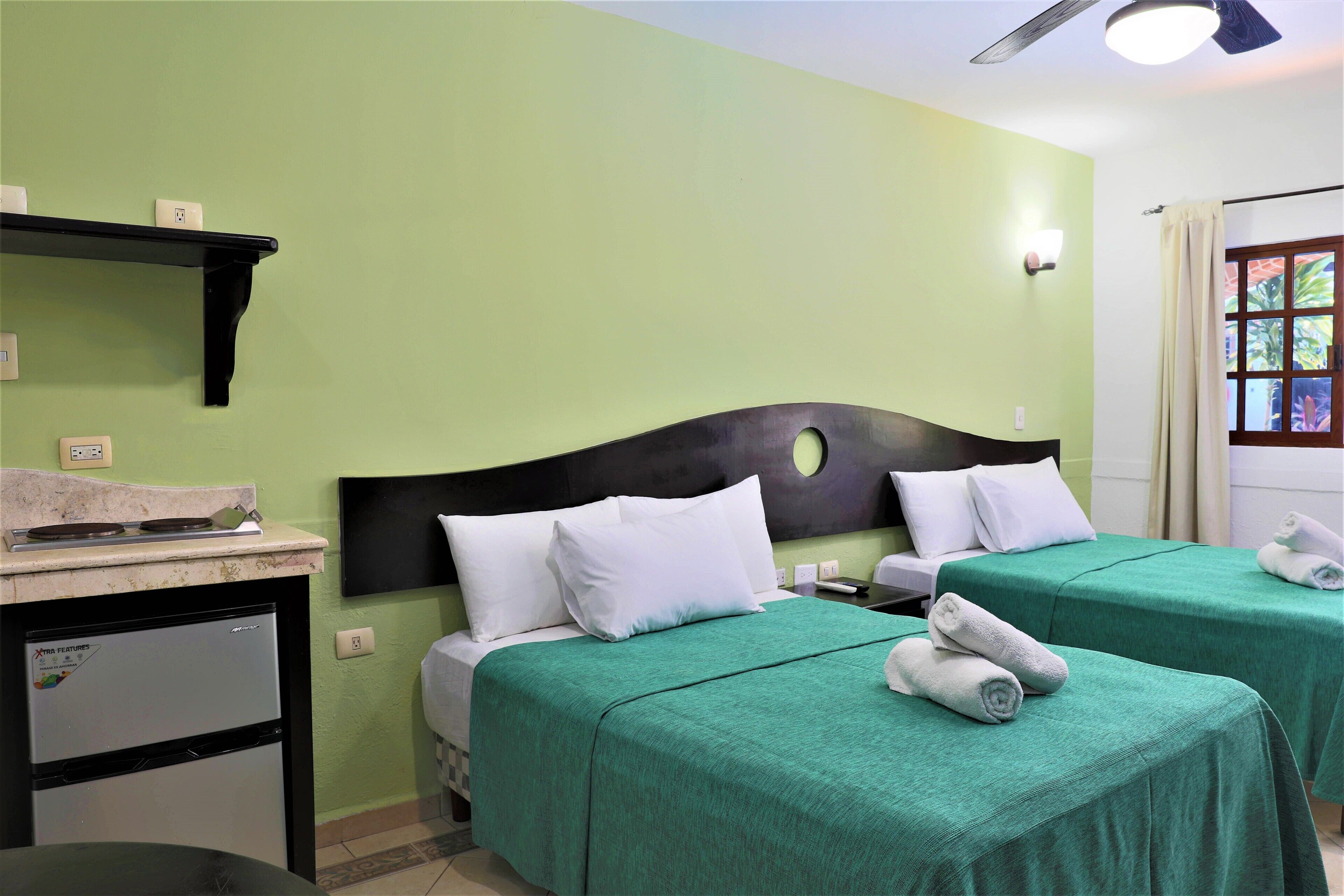 Habitación de hotel con dos camas, una kitchenette pequeña y un ventanal con cortinas.
