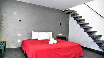 Quarto moderno com uma cama grande, um cobreleite vermelho, almofadas brancas, um banco de madeira e uma escada com degraus escuros.