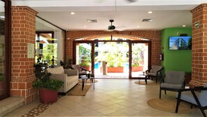 A lobby with a brick wall, a sofa, chairs, a ceiling fan, and a view of the outside.
