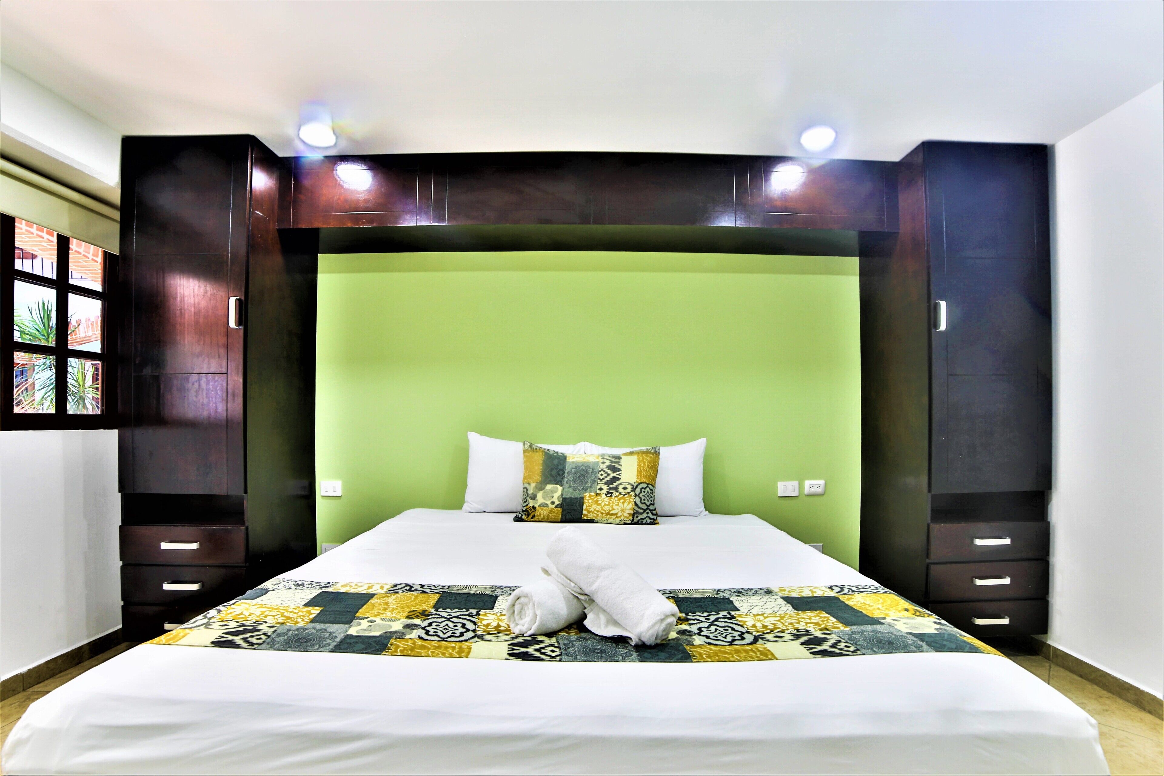 Una habitación de hotel con una cama grande, cabecera verde y muebles de madera oscura.