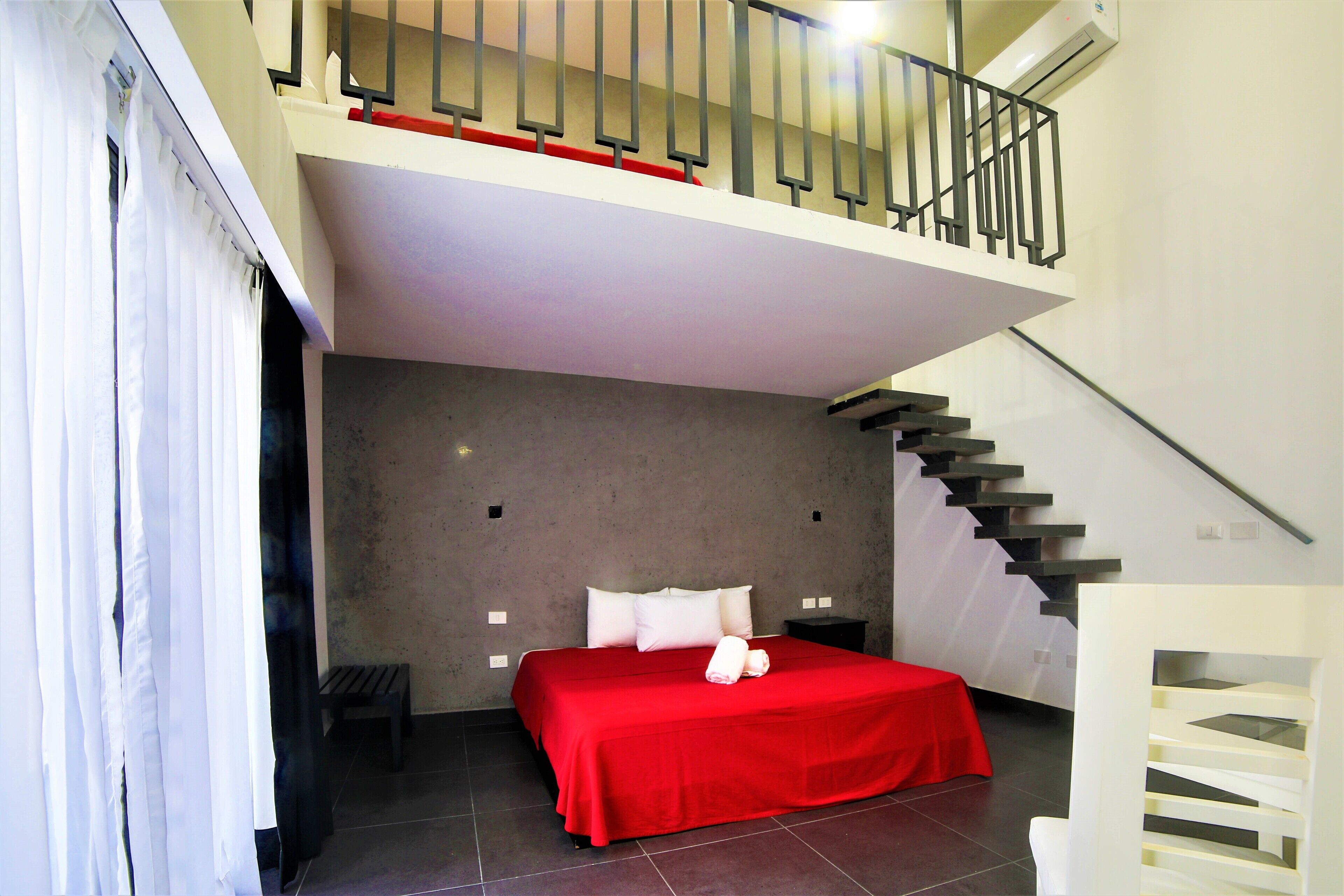 A bedroom with a red bedspread, a small bedside table, and a staircase leading to an upper level.
