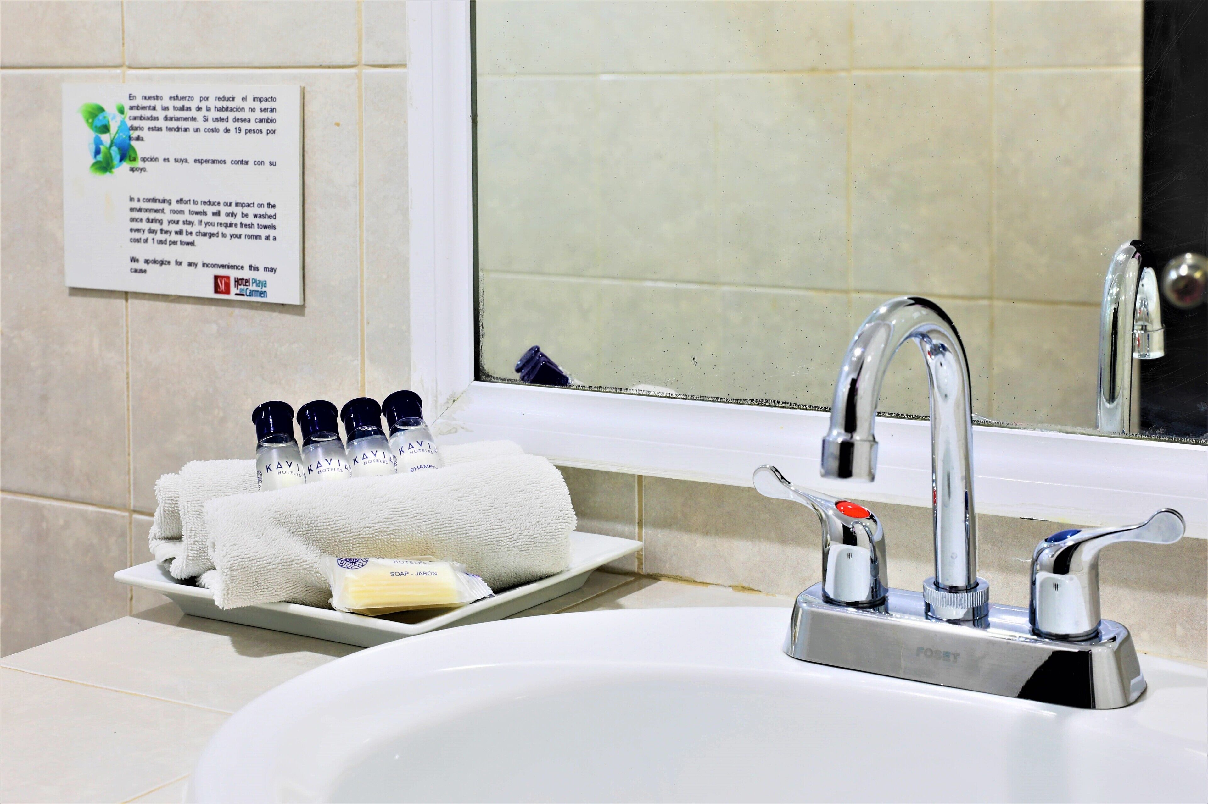 Un lavabo dans la salle de bain, avec un miroir au-dessus, un porte-serviettes avec des serviettes et des articles de toilette, et un panneau accroché au mur.