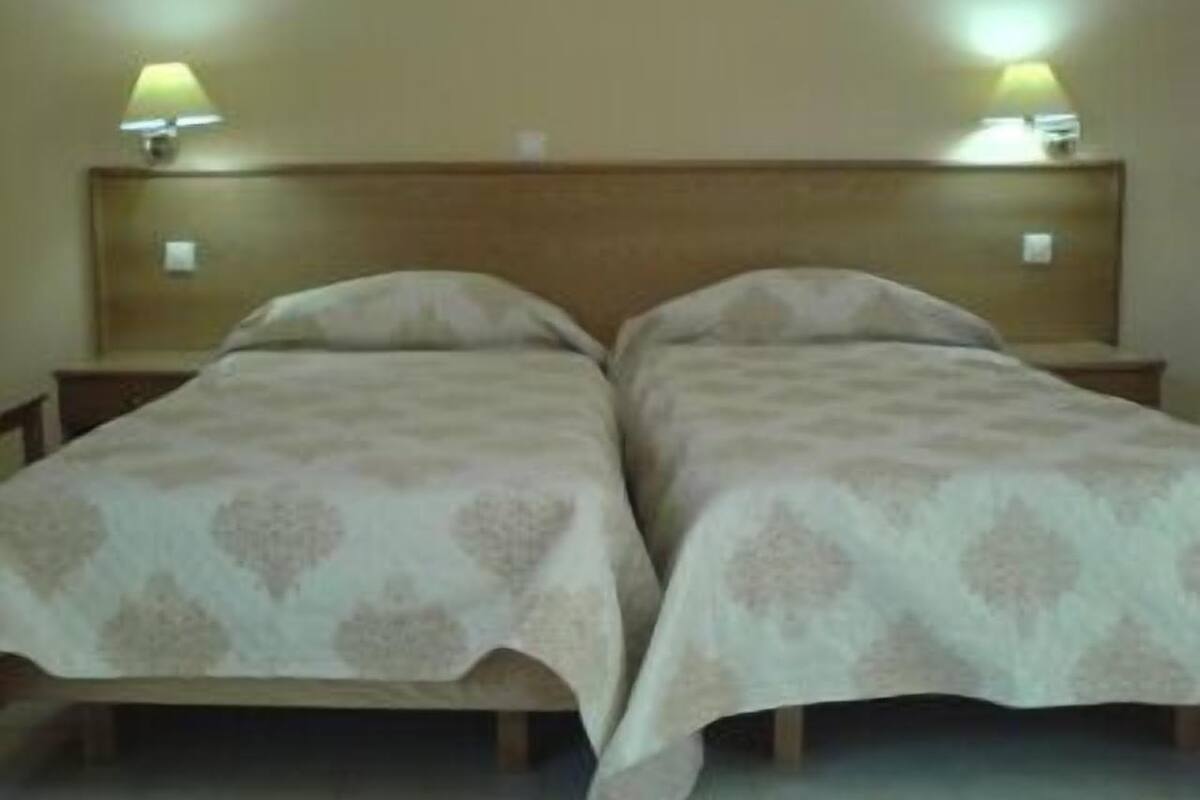 Een tweepersoonsbed met een houten hoofdbord, twee bedlampjes en een beddegoed met dessin.