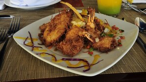 Ein Esstisch mit einem Teller frittiertem Essen, zwei Gläsern eines gelben Getränks und einer Schüssel mit Grissini.