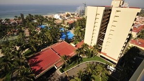 Ein Hochhaus-Hotel mit Poolbereich mit rotem Dach, Palmen und Blick auf Strand und Meer.