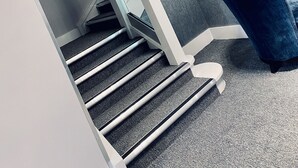 A modern staircase with a glass railing, carpeted steps, and a blue chair. - Dean Park Hotel (Kirkcaldy)