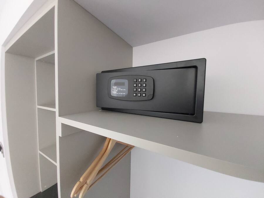 A black electronic keypad mounted on a white shelf in a room with a white wall and a wooden floor.