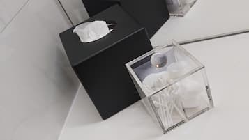 Pared de mármol blanco con tres cajas de pañuelos negros y un recipiente de vidrio transparente con hisopos.