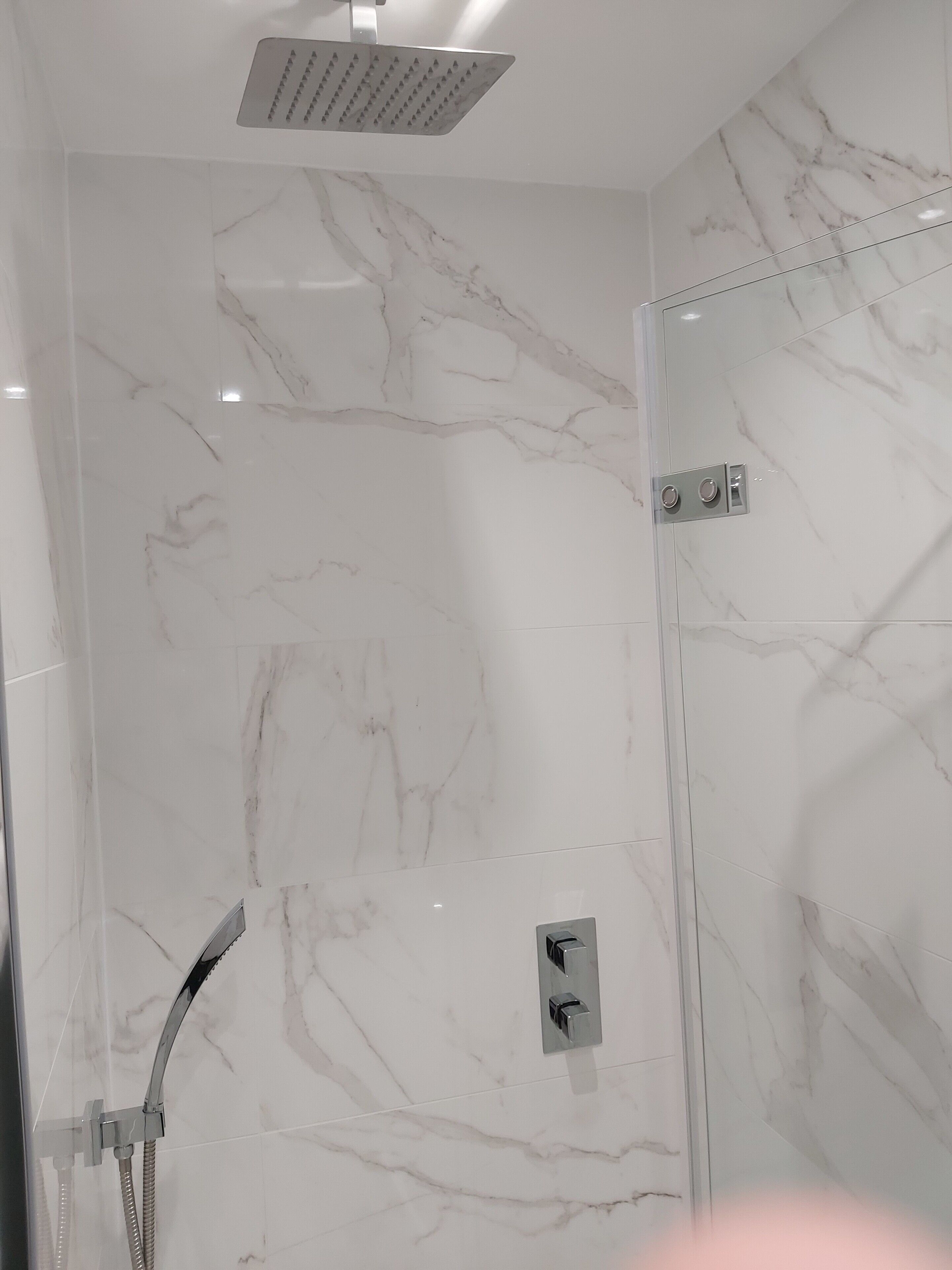 Una ducha moderna con cabezal de ducha de lluvia, un cabezal de ducha manual y un panel de control en la pared.