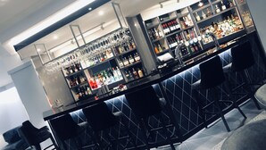 A bar area with multiple shelves of liquor bottles, bar stools, and a seating area with a patterned backrest. - Dean Park Hotel (Kirkcaldy)