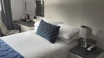 A hotel room with a bed, a bedside table with a lamp, a TV, and a chair.