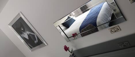 Ein Schlafzimmer mit einem Bett, einem Spiegel, einem kleinen Tisch mit einer Vase und einer Steckdose.