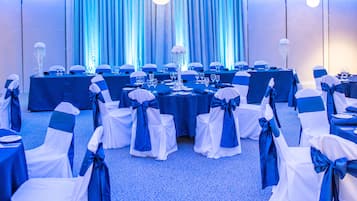 Un salón de banquetes con mesas dispuestas para un evento formal, cortinas azules y candelabros.