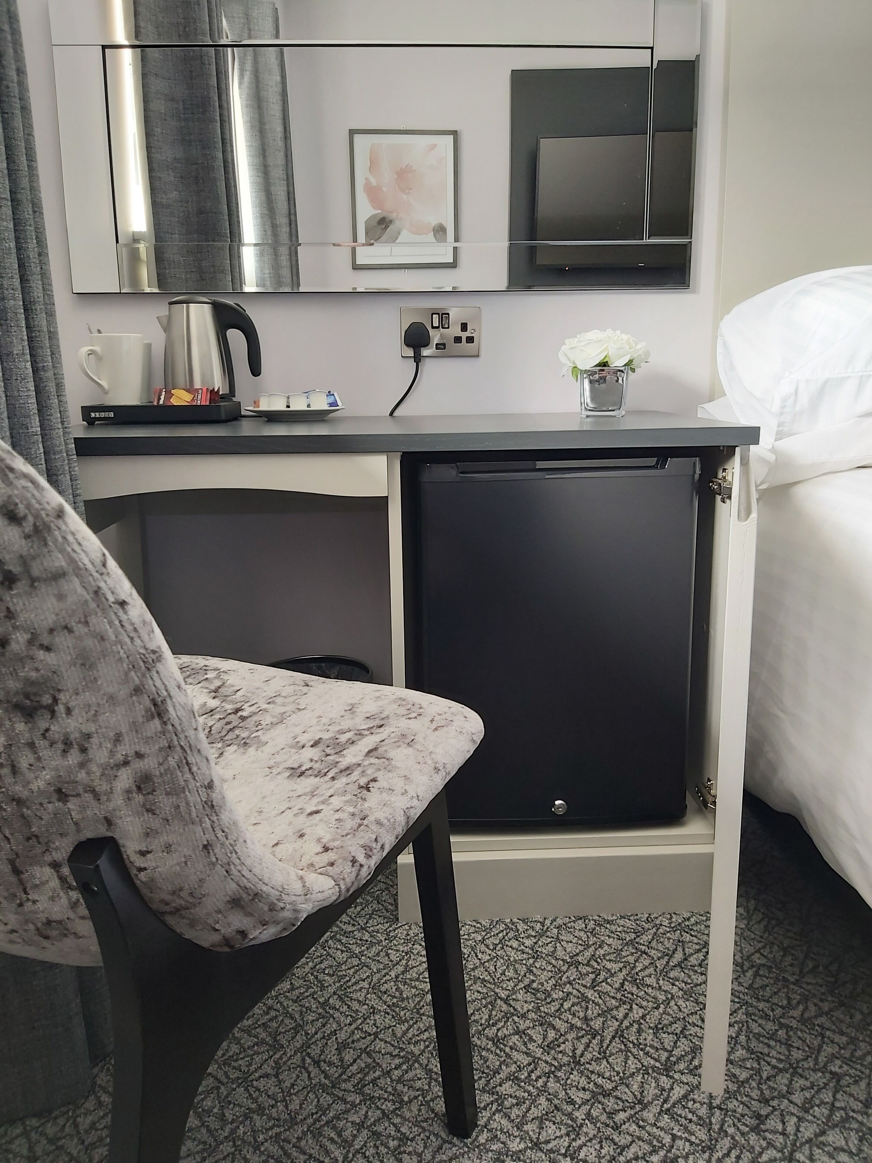 A compact hotel room with a small kitchenette, a single bed, and a marble-patterned chair.