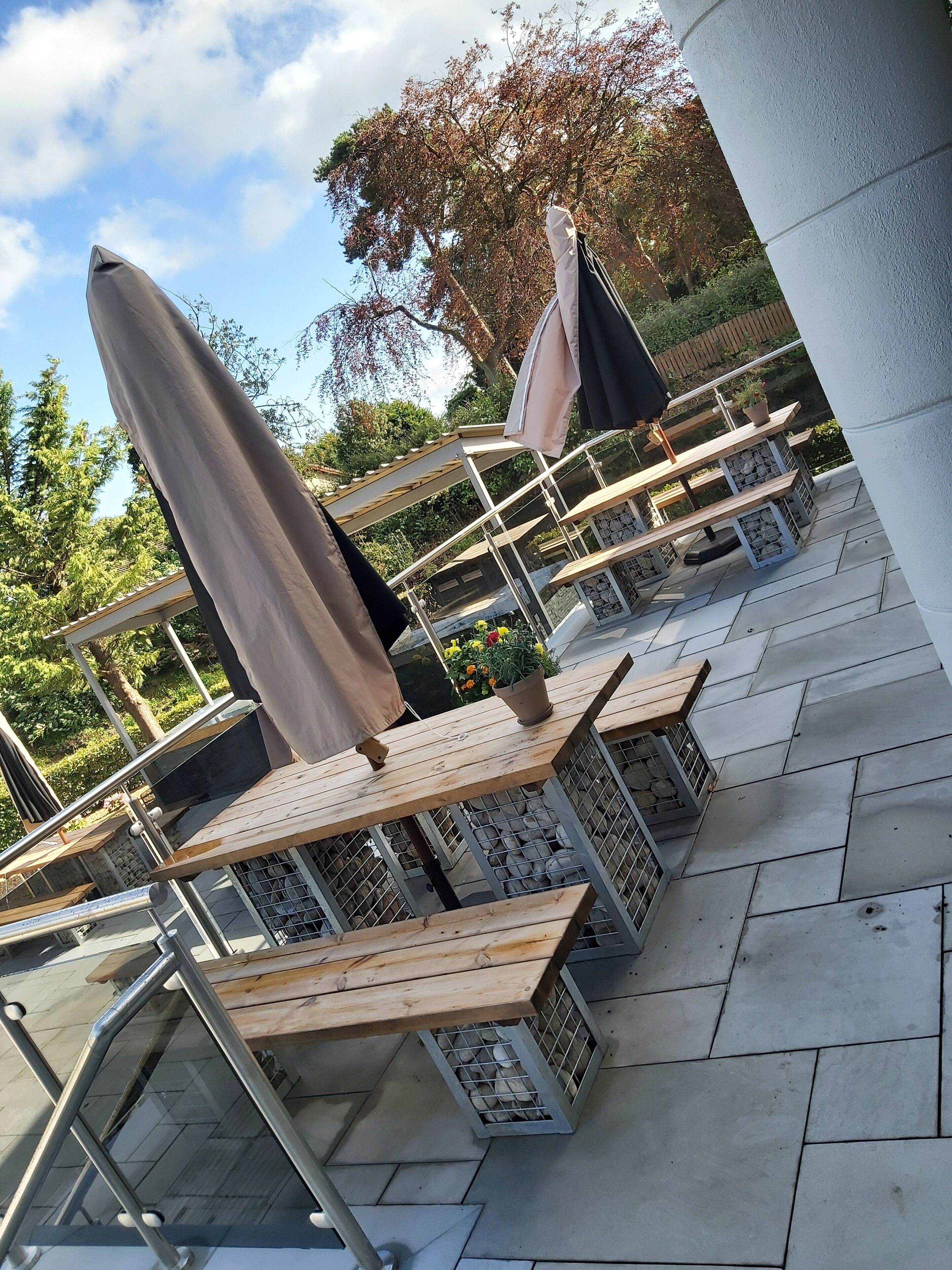 Espace extérieur aménagé avec des parasols, un sol en pierre et une vue sur les arbres et le ciel.