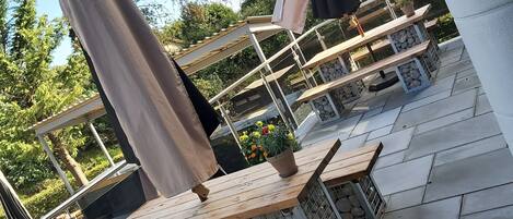 Espace extérieur aménagé avec des parasols, un sol en pierre et une vue sur les arbres et le ciel.