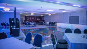 Ein Konferenzraum mit Tischen und Stühlen, eine Bühne mit Soundsystem und ein farbenfroher LED-Boden.