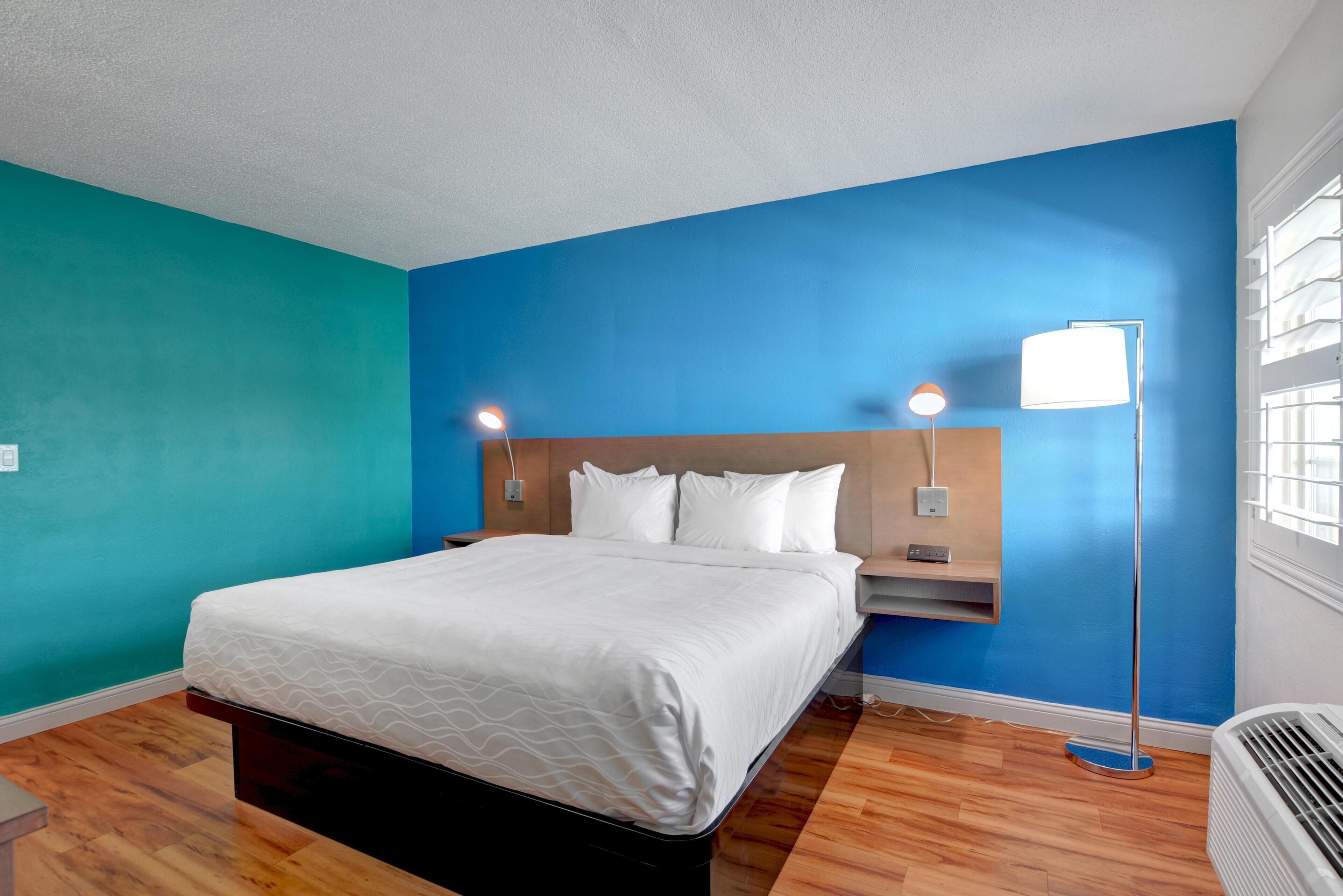 A hotel room with a bed, nightstands, a floor lamp, and a window with blinds.
