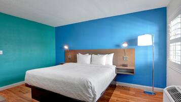 A hotel room with a bed, nightstands, a floor lamp, and a window with blinds.